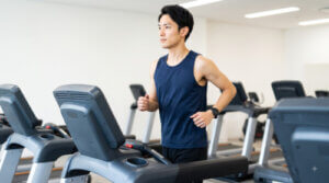 ジムの明るい有酸素エリアで、最新のランニングマシンを使い、真剣な表情でランニングをする日本人男性。