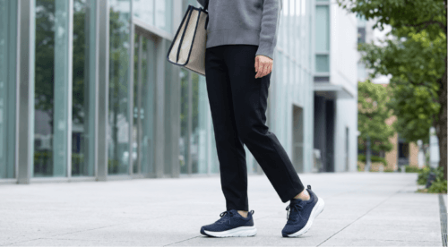都市部の歩道で、クッション性の高いネイビーのランニングシューズを履き、快適に歩くカジュアルな服装の日本人女性の足元。