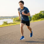 日夕の川沿いの舗装路を走る、厚底ランニングシューズを履いた日本人男性ランナーのダイナミックなストライド。