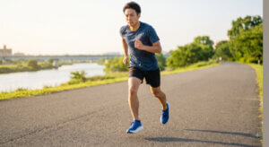 日夕の川沿いの舗装路を走る、厚底ランニングシューズを履いた日本人男性ランナーのダイナミックなストライド。