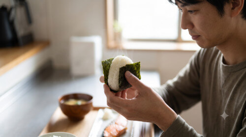 マラソン当日の朝食として、おにぎりを持つ日本人男性の手元のクローズアップ