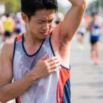 マラソン中、ウェアと擦れて赤くなった脇を痛そうにする日本人男性ランナー。摩擦トラブルの様子。