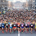 大規模な日本の市民マラソン大会のスタート地点で、大勢の日本人ランナーが密集して走り出す様子。男性ランナーが多数を占めている。