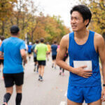 マラソン大会のコース上で、腹痛を抱えて苦しそうな表情で立ち止まる日本人男性ランナー。