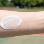 日本人の腕の肌に、白く濃厚なミルクタイプの日焼け止めと、透明でみずみずしいジェルタイプの日焼け止めが並べて塗布され、そのテクスチャーと肌なじみの違いを比較するクローズアップ写真。