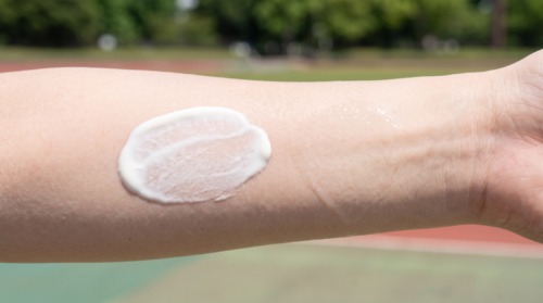 日本人の腕の肌に、白く濃厚なミルクタイプの日焼け止めと、透明でみずみずしいジェルタイプの日焼け止めが並べて塗布され、そのテクスチャーと肌なじみの違いを比較するクローズアップ写真。