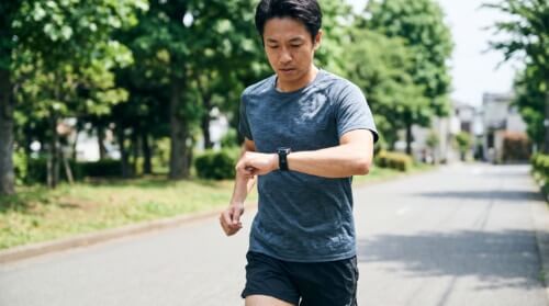 ランニング中に手首のスマートウォッチの画面を確認するアジア人男性ランナーの様子。日々のトレーニングでVO2maxなどのデータをチェックする日常風景。