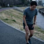 練習翌日に重い脚を引きずりながら、疲労感のある表情で走る日本人の男性ランナー。