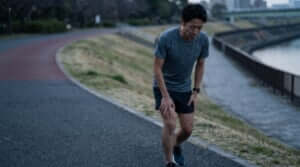 練習翌日に重い脚を引きずりながら、疲労感のある表情で走る日本人の男性ランナー。