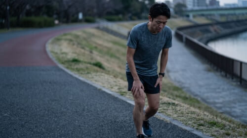練習翌日に重い脚を引きずりながら、疲労感のある表情で走る日本人の男性ランナー。